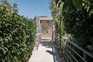 A pathway leading to a stone structure with a metal gate, surrounded by dense foliage. - Olimpia Villas (Apokoronas)