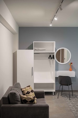 A modern room with a grey sofa, a white wardrobe, a round mirror, and a small desk with a vase. - Olimpia Villas (Apokoronas)