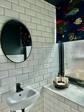 A bathroom with white subway tiles, a round mirror, a white sink, and a window with a view of fish. - Haugh Hideaway, Inverness (Inverness)