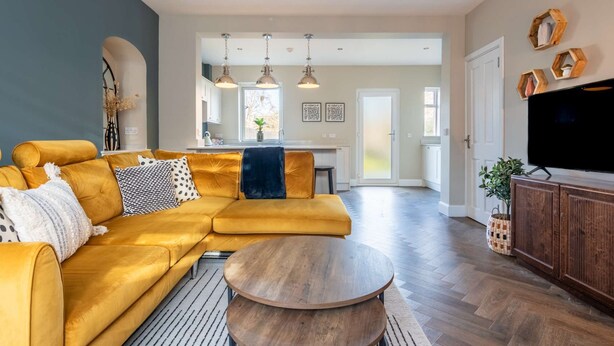 Uma sala de estar moderna com um sofá amarelo, uma mesa de centro redonda de madeira e uma TV sobre um armário de madeira.