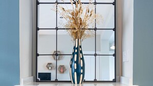 Um quarto com lareira branca, parede azul, poltrona amarela e janela com moldura metálica decorativa.