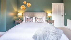 Quarto com uma cama grande, duas mesas de cabeceira com abajures, uma porta e três objetos decorativos na parede.