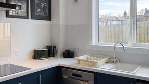 Cozinha moderna com lava-louças, pia e janela com vista para uma área residencial.