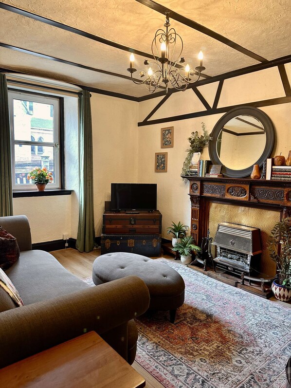 Una sala de estar con sofá, reposapiés, chimenea, televisor y una araña.