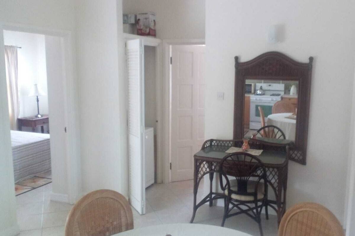 A dining area with a table and chairs, a mirror on the wall, and a door leading to another room.