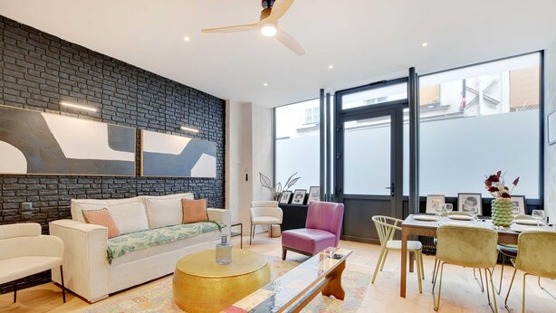 Een moderne woonkamer met een bakstenen muur, een bank, een salontafel en een eethoek met stoelen en een tafel gedekt voor een maaltijd.