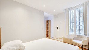 Een slaapkamer met een groot bed, een stoel, een kledingkast en een raam.