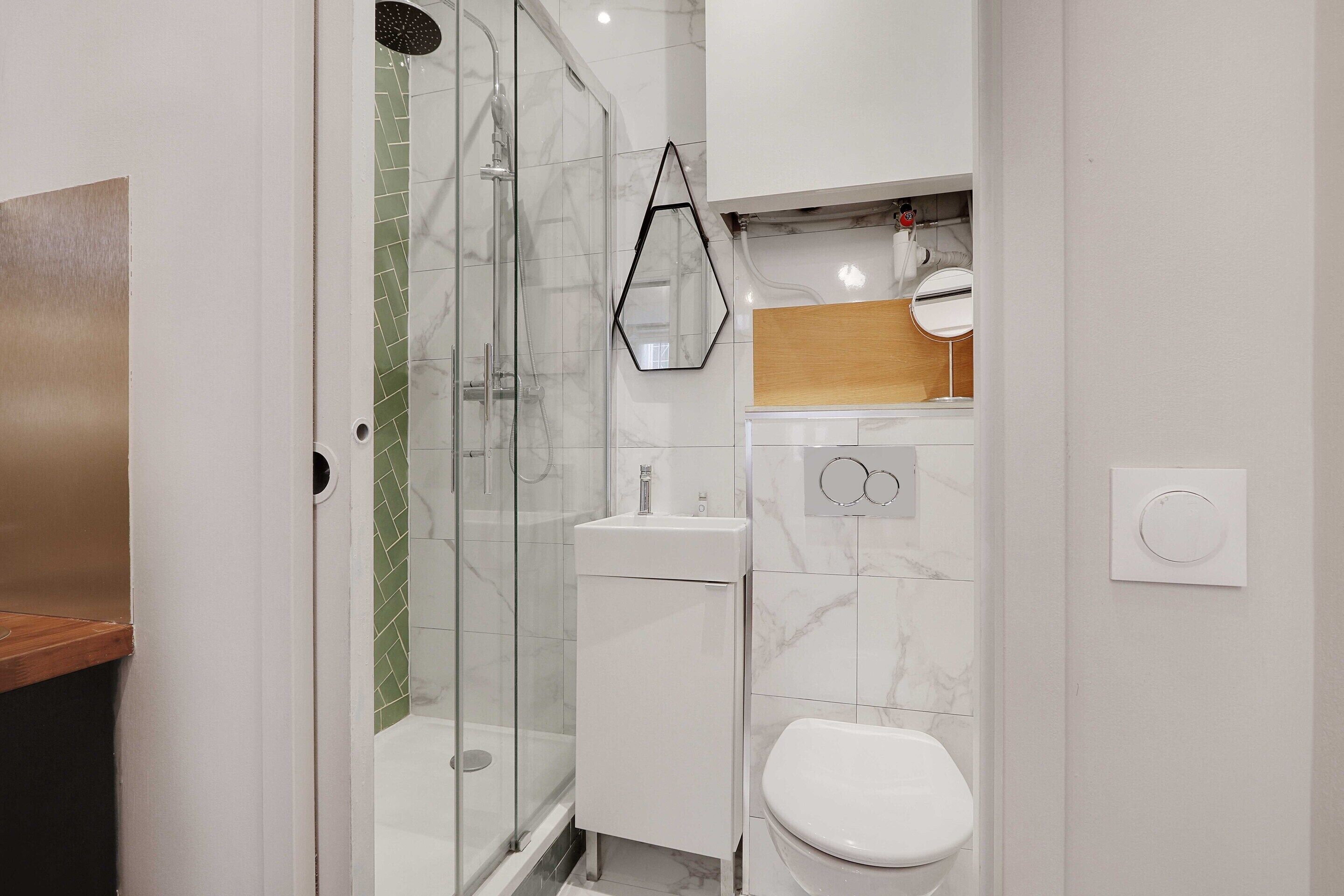 Een moderne badkamer met een douchecabine van glas, een witte wastafel en een toilet.