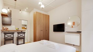 Een hotelkamer met een bed, twee stoelen, een houten garderobe, een spiegel en een televisie.