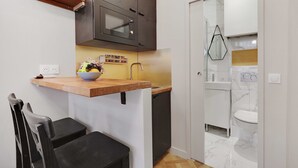 Een compacte keuken met een magnetron, een spoelbak en een klein eethoekje met een stoel.
