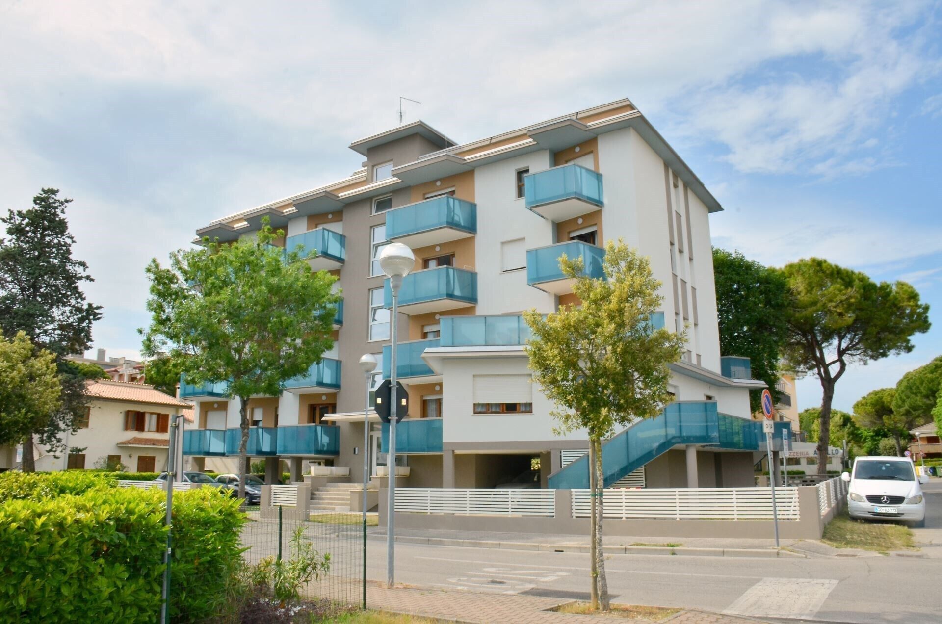 Um edifício residencial com vários andares, varandas, área de estacionamento e uma passarela para pedestres.