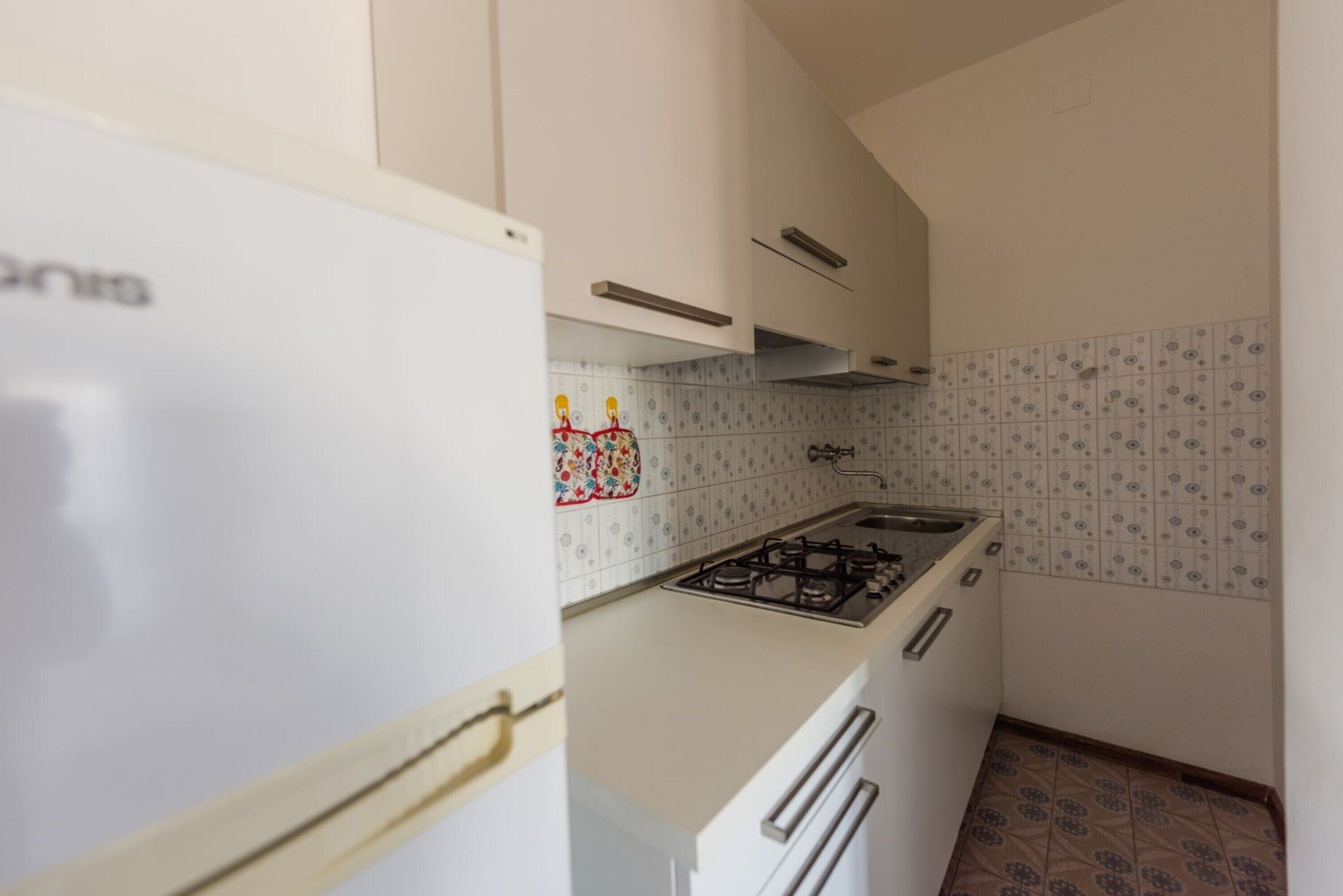 Una cocina compacta con estufa a gas, armarios blancos y azulejos decorativos en la pared.
