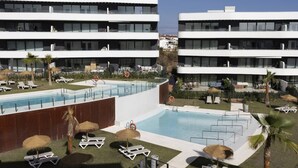 Un hôtel moderne doté d’une piscine sur le toit, de chaises longues et d’un jardin bien entretenu.