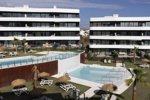 A modern hotel with a rooftop pool, lounge chairs, and a well-maintained garden.