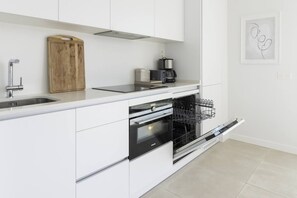 A modern kitchen with white cabinetry, a stainless steel sink, a wooden cutting board, a coffee maker, and a dishwasher. - Elegant Luxury Suite with Terrace in Higueron (Fuengirola)