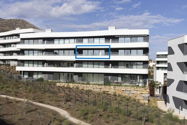 A multi-story building with a flat roof, large windows, and a stone retaining wall.