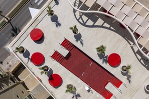 An aerial view of a rooftop terrace with a red seating area, potted plants, and a curved white structure. - Stunning Seafront Apartment in Carvajal Beach (Fuengirola)