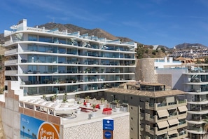 A multi-story hotel with balconies, a pool area, and a view of the surrounding landscape. - Stunning Seafront Apartment in Carvajal Beach (Fuengirola)