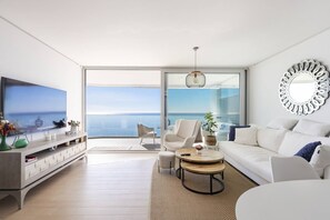 Een moderne woonkamer met een grote televisie, een bank, een salontafel en uitzicht op zee.