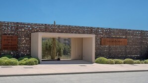 A modern building entrance with a stone facade, a clear sky, and a sign listing amenities like a hotel, sports club, spa, and restaurants. - Exclusive Apartment with Garden in Higueron (Fuengirola)