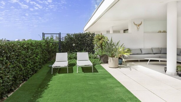 A modern outdoor space with two lounge chairs, a grey sofa, and a variety of potted plants. - Exclusive Apartment with Garden in Higueron (Fuengirola)
