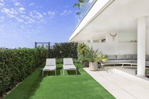 Un espace extérieur moderne comprenant deux fauteuils de relaxation, un canapé gris et une variété de plantes en pot.