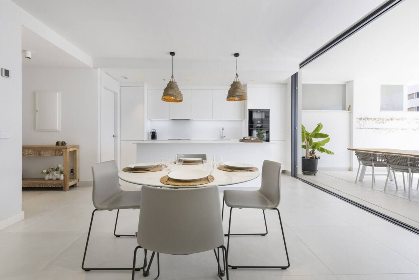 Une cuisine moderne avec des meubles blancs, une table à manger pour quatre personnes et des luminaires suspendus.