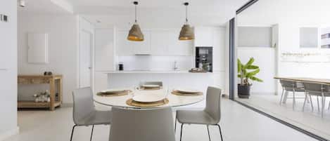 Une cuisine moderne avec des meubles blancs, une table à manger pour quatre personnes et des luminaires suspendus.
