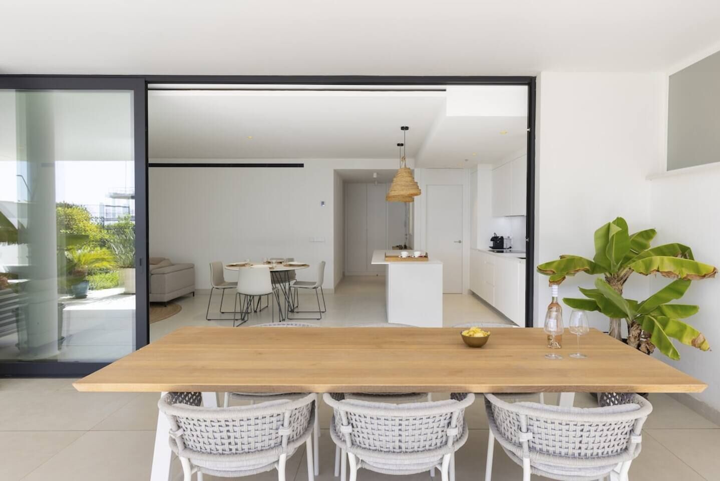 A modern kitchen with white cabinets, a wooden dining table, and a hanging light fixture.