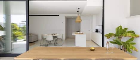 A modern kitchen with white cabinets, a wooden dining table, and a hanging light fixture.