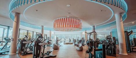 A modern gym with cardio machines, free weights, and a central circular design with a hanging light fixture.