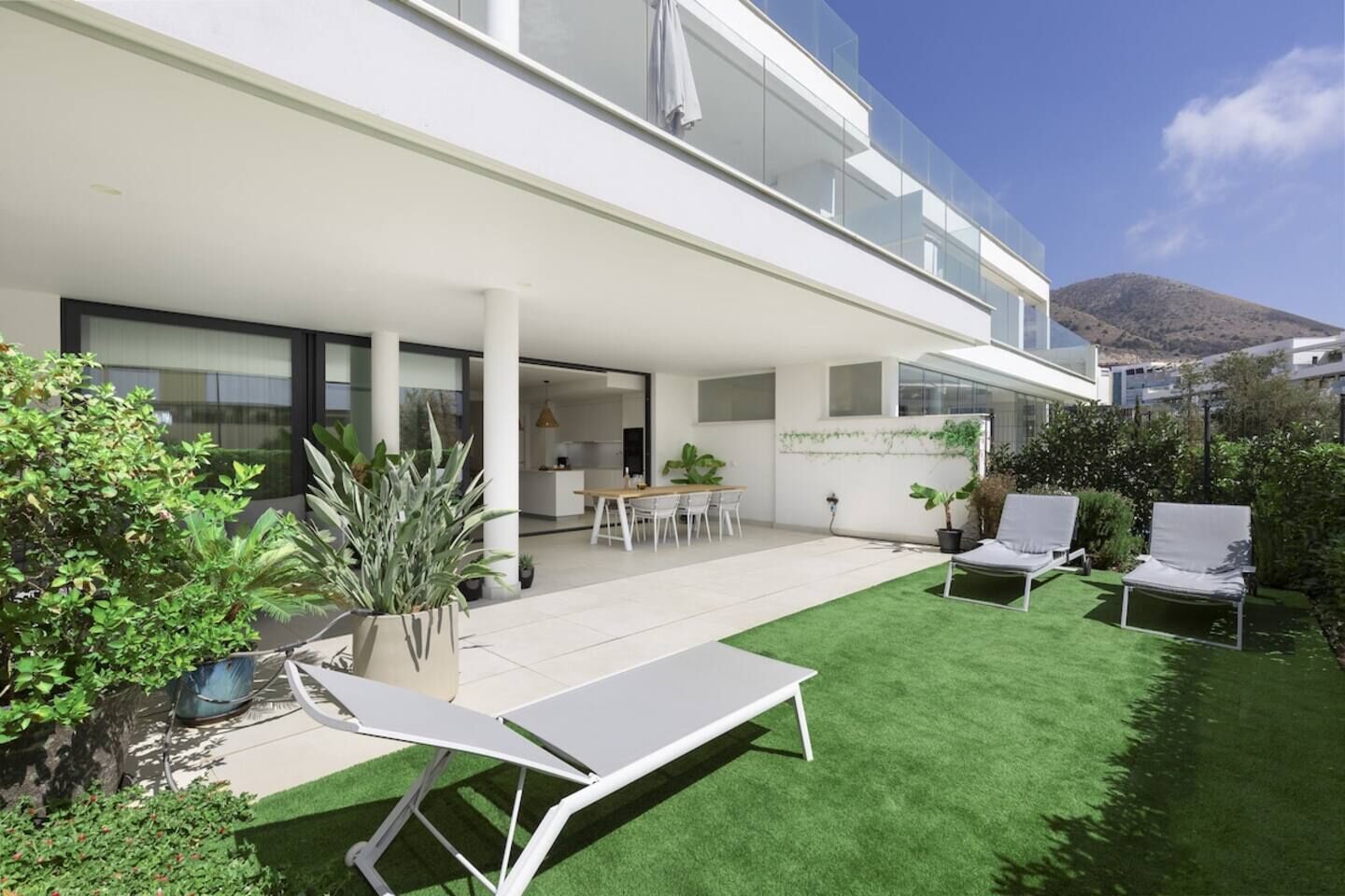 A modern building with a covered patio area, a dining table, and lounge chairs.