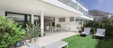 A modern building with a covered patio area, a dining table, and lounge chairs.