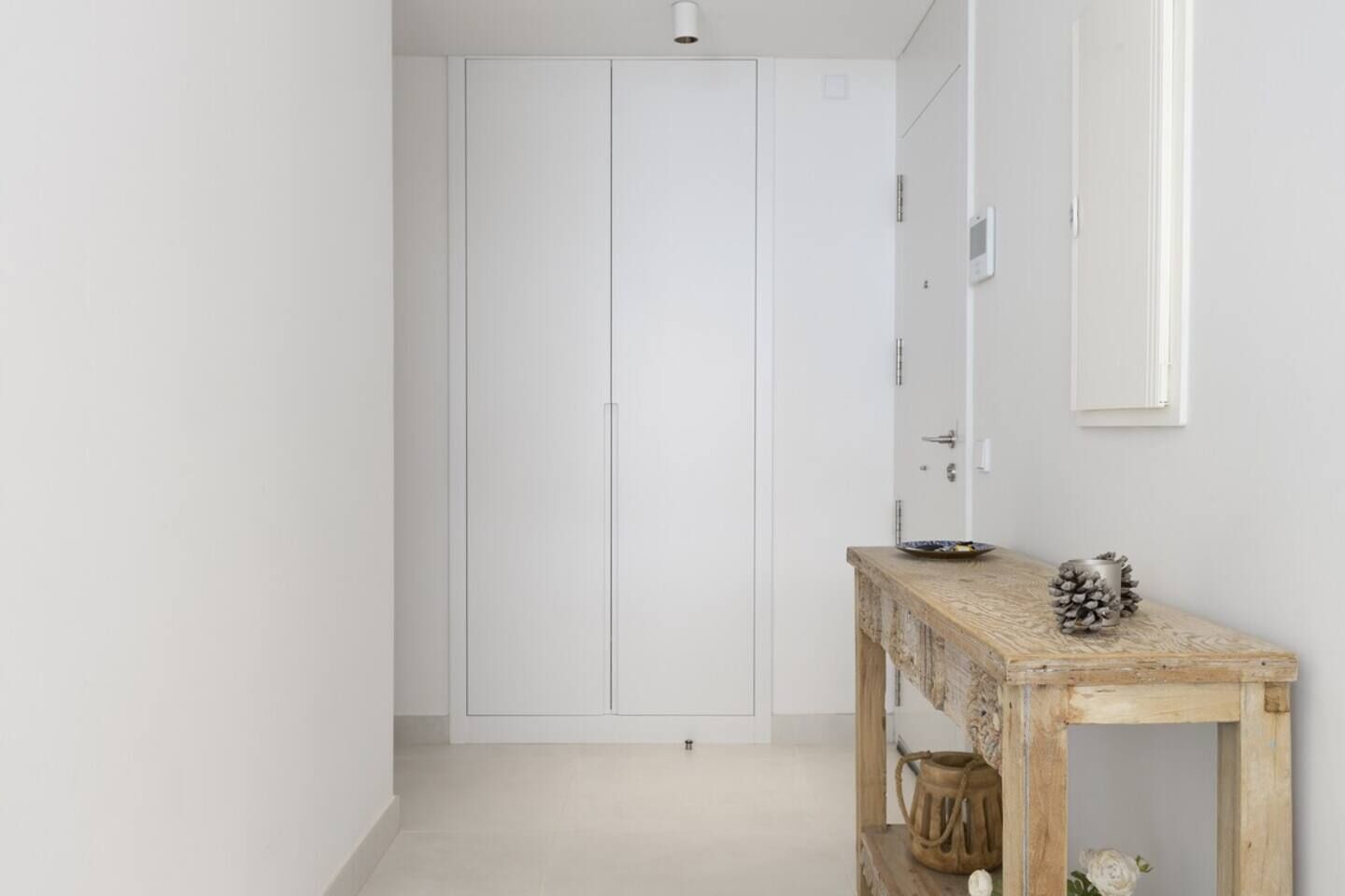 A hallway with a white wardrobe, a wooden console table with decorative items, and a white door.
