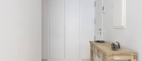 A hallway with a white wardrobe, a wooden console table with decorative items, and a white door.