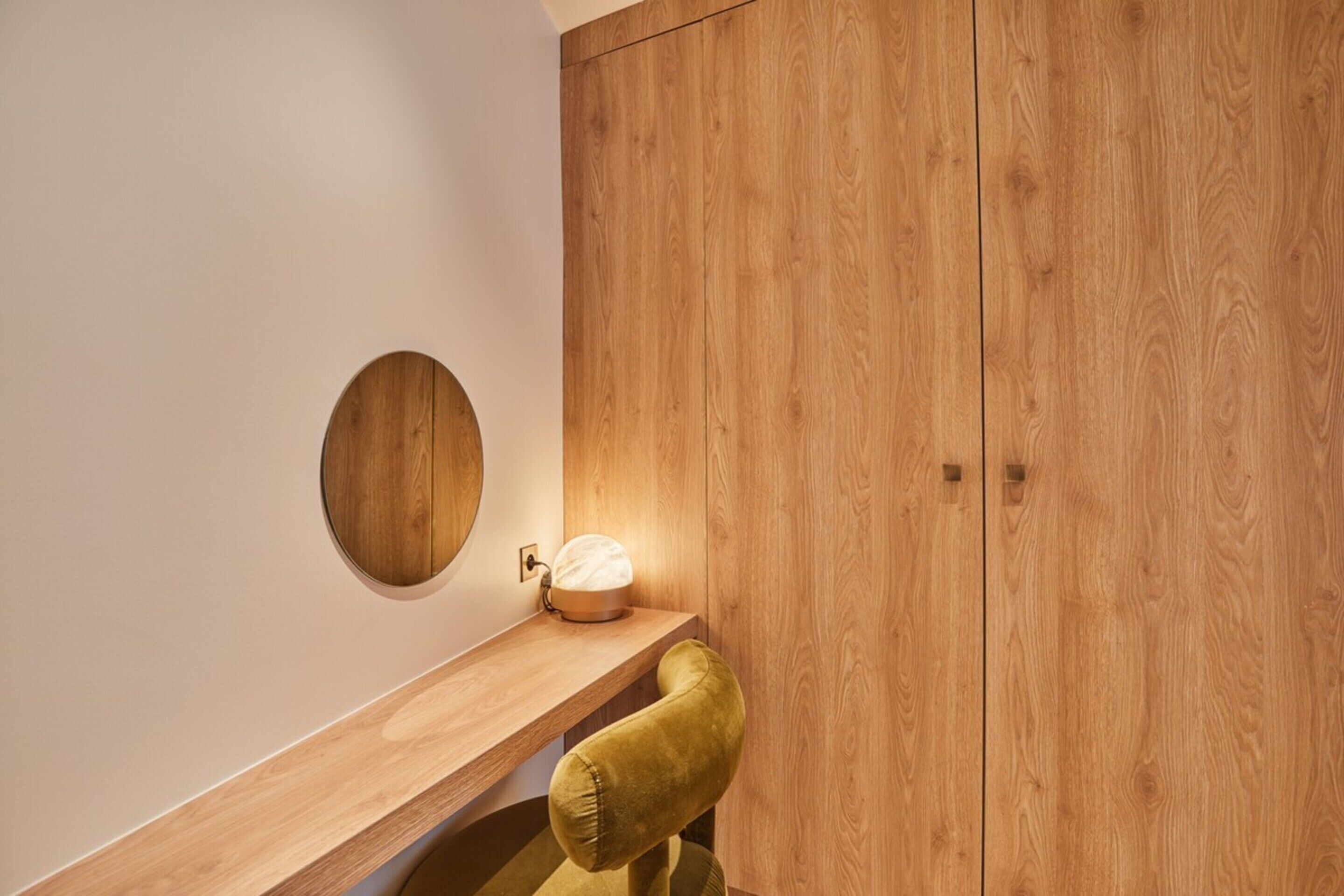 Ein modernes Badezimmer mit einem Holzbadezimmermöbel, einem runden Spiegel und einer Beleuchtung.