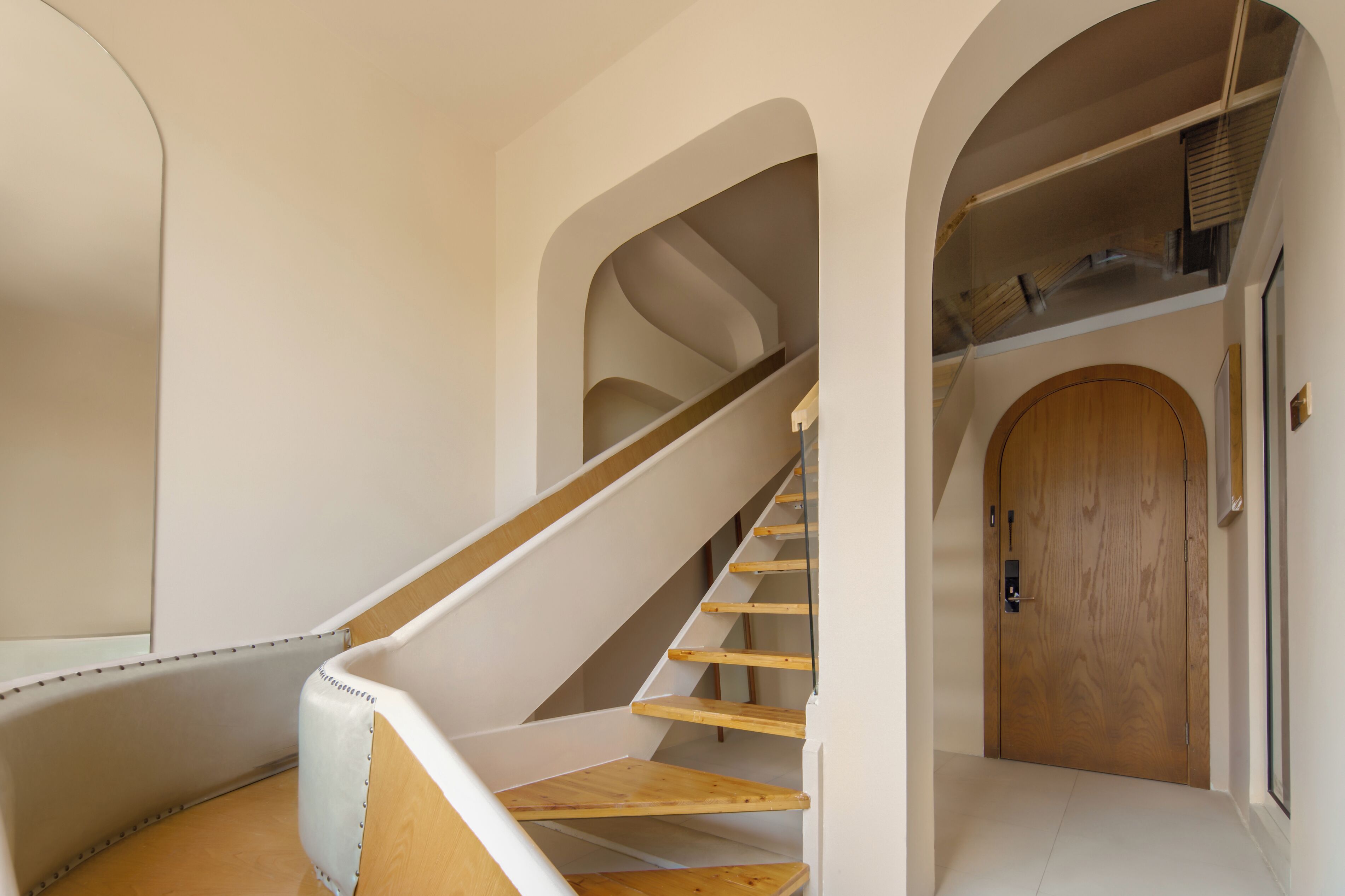 A modern interior with a wooden staircase, white walls, and a wooden door.