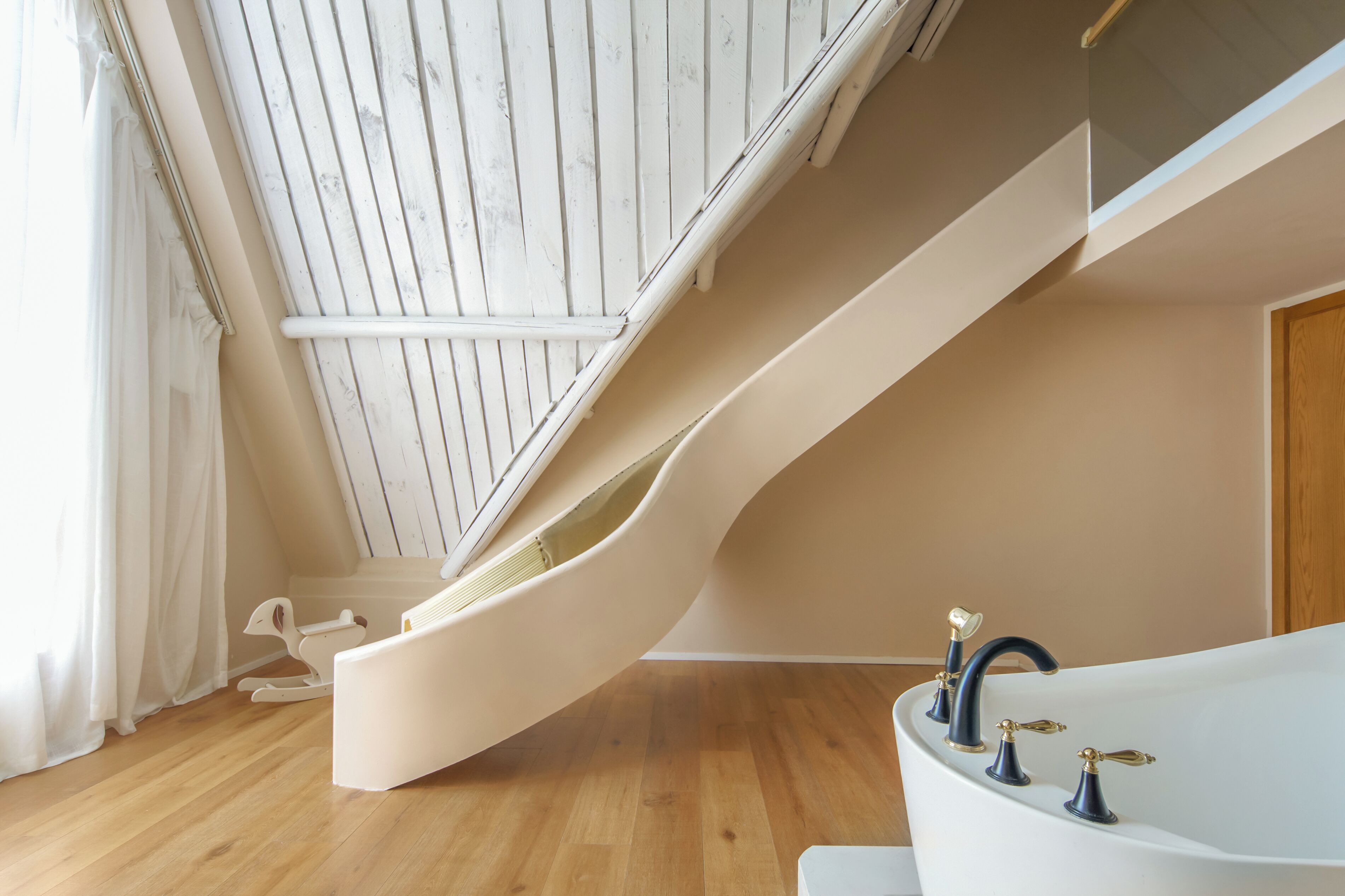 A room with a wooden floor, a white bathtub with gold fixtures, and a white sliding door.