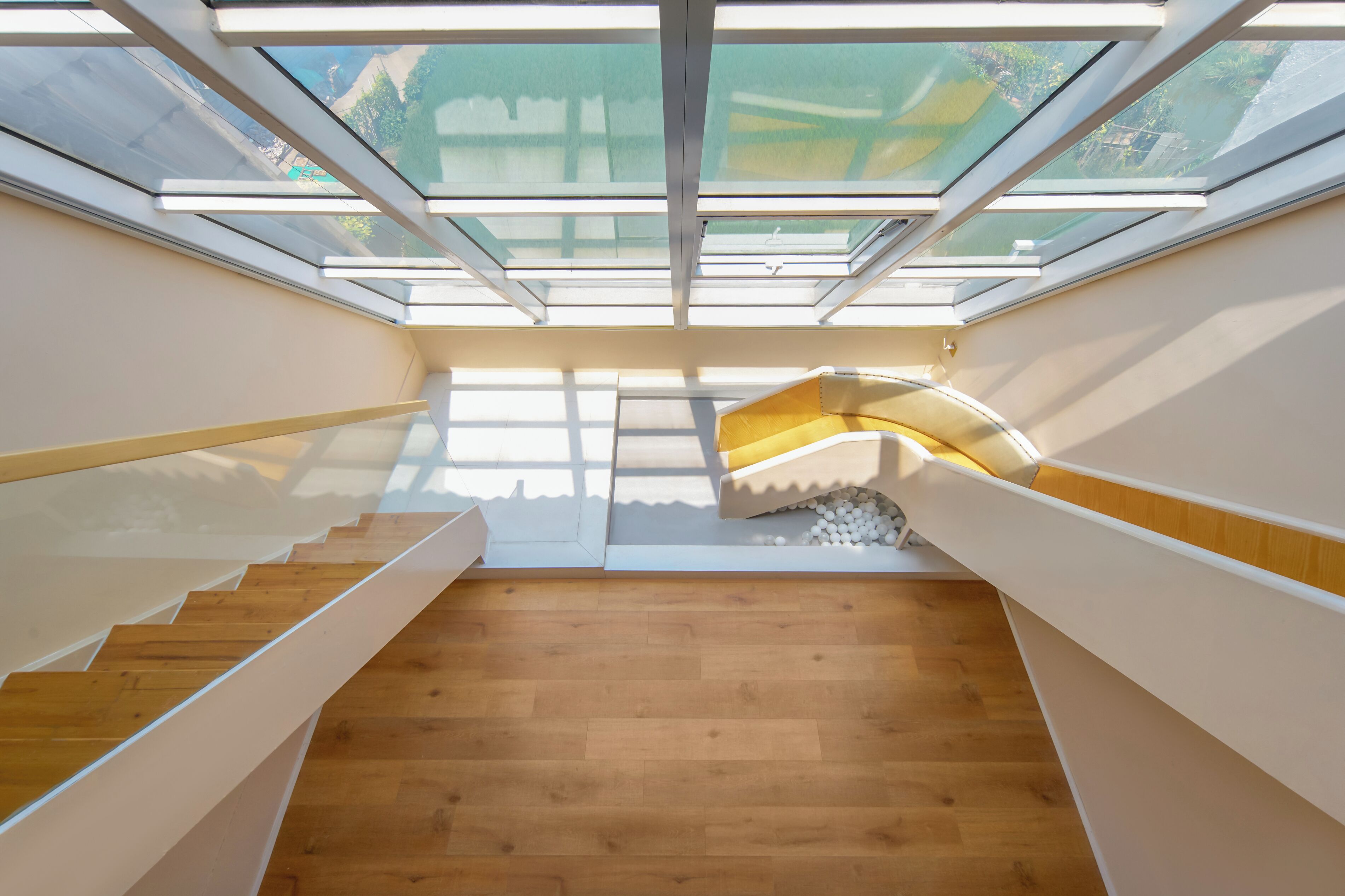 Un interior moderno con escalera de madera, tragaluces y barandilla blanca.