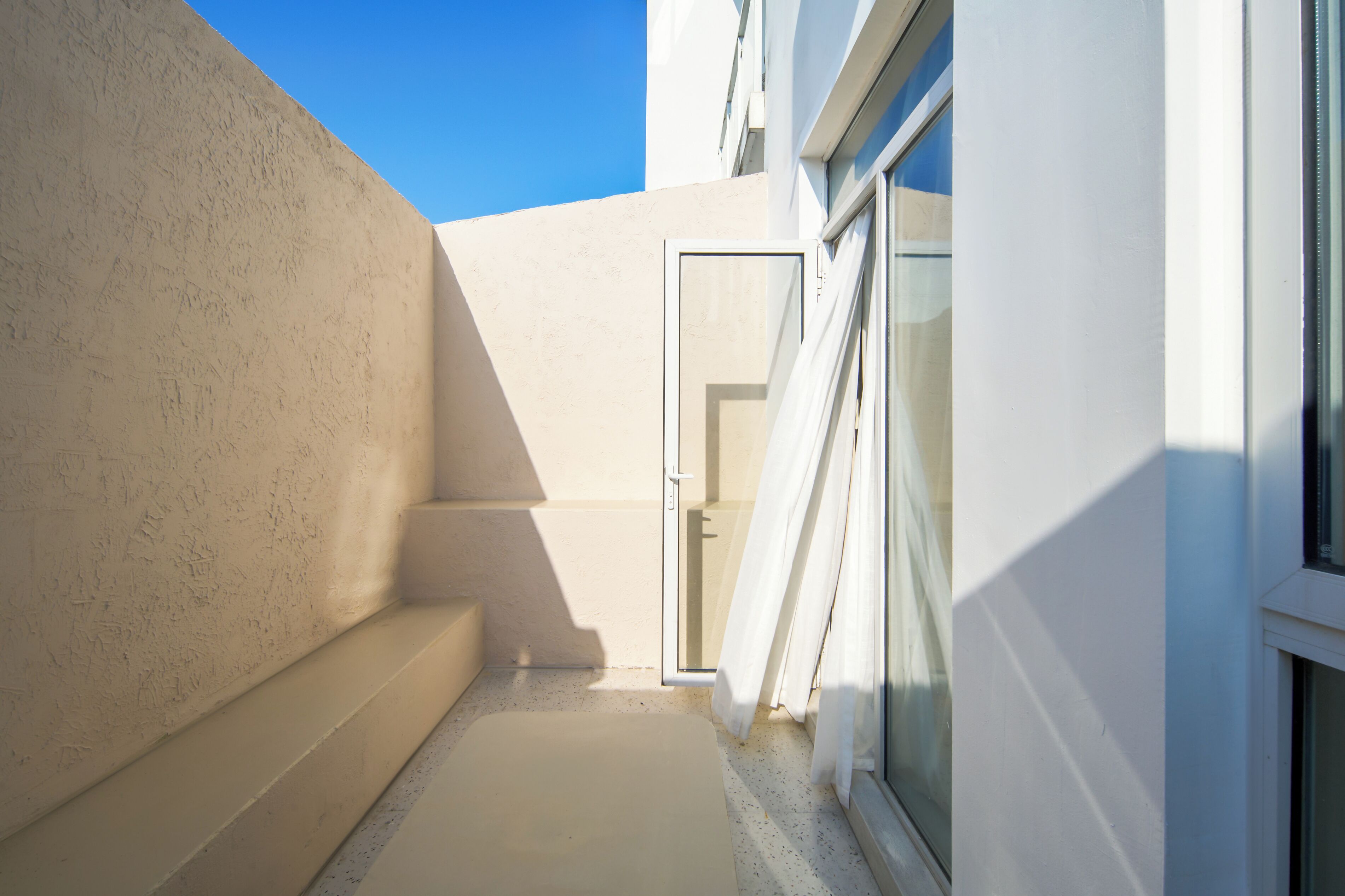 A narrow outdoor corridor with a glass door leading to a room.
