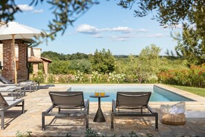Un espace aménagé au bord de la piscine, avec deux chaises longues, une table avec des boissons, et une vue sur un jardin paysager et la piscine.
