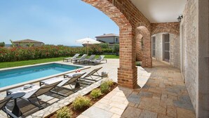 Un espace aménagé au bord de la piscine, avec une arche en briques, des chaises longues et une vue dégagée sur la mer.