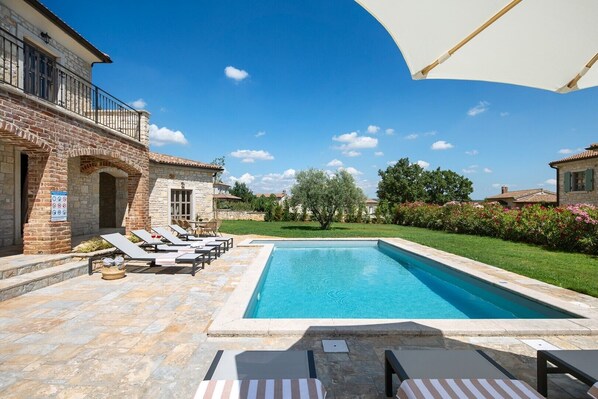 A swimming pool with lounge chairs and a stone building with a balcony.