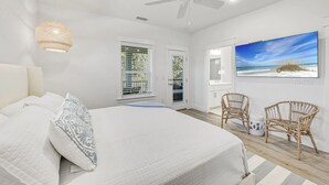 A bedroom with a large bed, two wicker chairs, a ceiling fan, and a beach view painting. - Newly Built • Pool Access + Golf Cart Walk to Beach | 30A Ocean Pearl (Santa Rosa Beach)