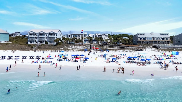 A beach with multiple umbrellas, people, and buildings in the background. - Newly Built • Pool Access + Golf Cart Walk to Beach | 30A Ocean Pearl (Santa Rosa Beach)
