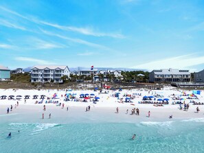 Een strand met meerdere parasols, mensen en gebouwen op de achtergrond.