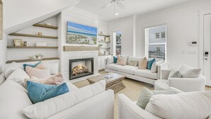 A modern living room with a fireplace, white sofas, and a ceiling fan. - Newly Built • Pool Access + Golf Cart Walk to Beach | 30A Ocean Pearl (Santa Rosa Beach)