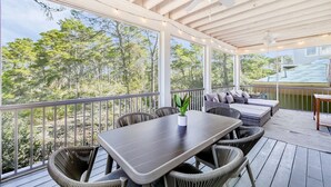 A covered outdoor area with a table and chairs, a sofa, and a railing overlooking a forested area. - Newly Built • Pool Access + Golf Cart Walk to Beach | 30A Ocean Pearl (Santa Rosa Beach)