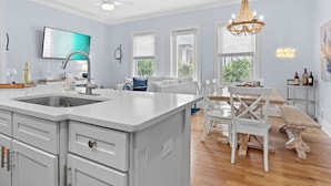 A modern kitchen with a large island, white cabinetry, and a dining area with white chairs and a wooden table.