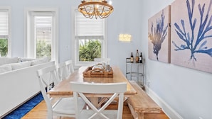 A dining area with a wooden table, white chairs, a chandelier, and artwork on the wall.
